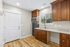 Second kitchen in the basement with stainless steel microwave, light wood-style floors, light countertops, recessed lighting, and brown cabinets