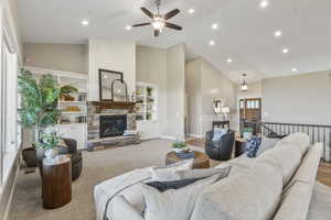 Living room featuring high vaulted ceiling, ceiling fan, recessed lighting, a stone fireplace, and carpet flooring