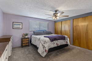 Carpeted bedroom featuring two closets, ceiling fan, and a textured ceiling