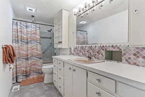 Bathroom featuring vanity, shower / bath combo with shower curtain, decorative backsplash, and a textured ceiling