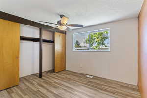 Unfurnished bedroom with wood finished floors, a closet, a textured ceiling, and ceiling fan
