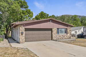 View of front of property with stone siding, an attached garage, concrete driveway, and a mountain view