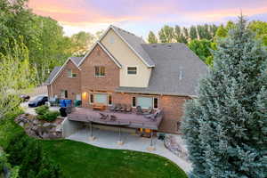 Back of house at dusk featuring a deck, brick siding, a patio, and a yard