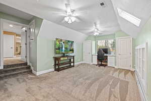 Home office featuring a ceiling fan, light carpet, lofted ceiling, and skylight,.
