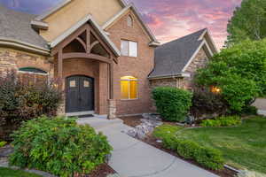Property entrance featuring a yard, brick siding, roof with shingles, and stone siding