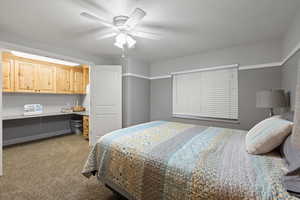 Carpeted bedroom featuring ceiling fan and built in desk