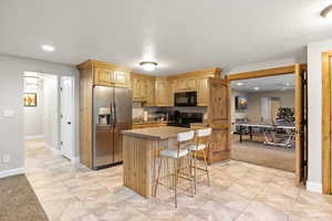 Kitchen with black appliances, a kitchen island, light carpet, recessed lighting, and a breakfast bar area