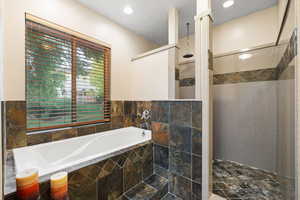 Bathroom featuring a bath, walk in shower, tile walls, stone flooring, and recessed lighting