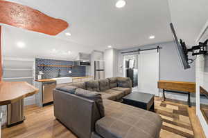 Living room with a textured ceiling, a barn door, light wood-style flooring, wet bar, and recessed lighting