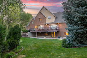 Back of house featuring a patio, a wooden deck, brick siding, a yard, and stucco siding