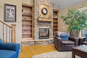 Living room featuring wood finished floors, a fireplace, vaulted ceiling, built in features, and stairway