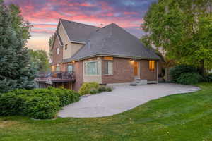 Back of property at dusk with a shingled roof, brick siding, and a lawn