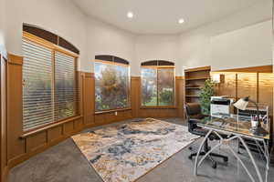 Carpeted office featuring a wainscoted wall, recessed lighting, a decorative wall, and a towering ceiling
