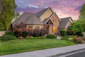 View of front of property with a lawn, stone siding, roof with shingles, and stucco siding