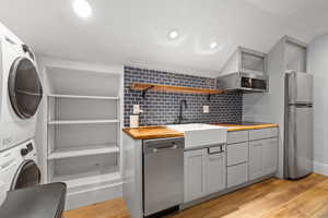 Kitchen featuring appliances with stainless steel finishes, butcher block counters, stacked washer / drying machine, gray cabinets, and tasteful backsplash