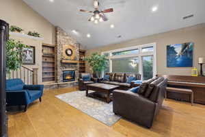Living room with high vaulted ceiling, a ceiling fan, light wood finished floors, a stone fireplace, and recessed lighting