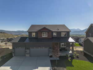 View of front of property featuring covered porch, a standing seam roof, a mountain view, concrete driveway, and a metal roof