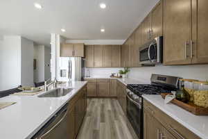 Kitchen featuring appliances with stainless steel finishes, light countertops, light wood finished floors, recessed lighting, and brown cabinets