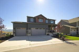 Townhome / multi-family property featuring concrete driveway, an attached garage, stone siding, and covered porch