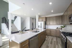 Kitchen featuring stainless steel appliances, light wood-style floors, a center island with sink, light countertops, and recessed lighting