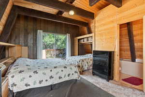 Carpeted bedroom with wood walls and a wooden ceiling with exposed beams