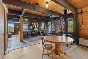 Tiled dining area featuring a wooden ceiling with exposed beams, wooden walls, heating unit, and stairs