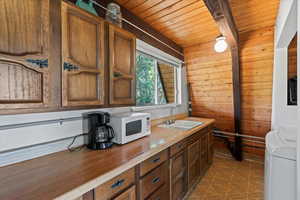 Kitchen with washer / dryer, white microwave, wooden ceiling, wooden walls, and light countertops