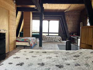 Carpeted bedroom with wood walls and a wooden ceiling with exposed beams
