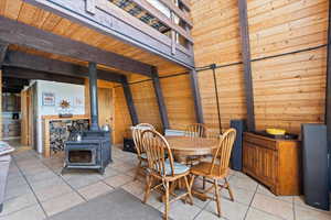 Dining room with a wood stove, wood walls, light tile patterned floors, and beamed ceiling