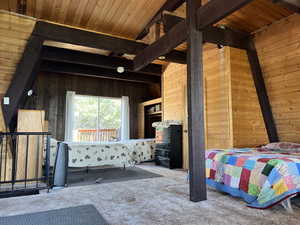 Carpeted bedroom featuring beam ceiling and wooden walls
