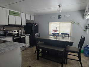 Kitchen with black appliances, white cabinets, under cabinet range hood, and light countertops