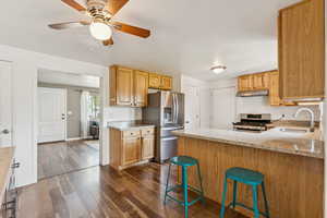 Kitchen with appliances with stainless steel finishes, under cabinet range hood, light stone counters, and a peninsula