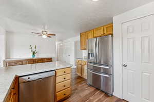 Kitchen with stainless steel appliances, dark wood finished floors, a ceiling fan, a textured ceiling, and light stone counters