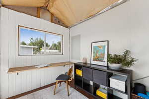 Home office featuring lofted ceiling and wood walls