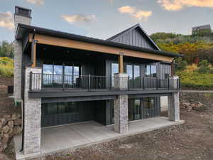 Back of house featuring board and batten siding, stone siding, a patio area, and a chimney