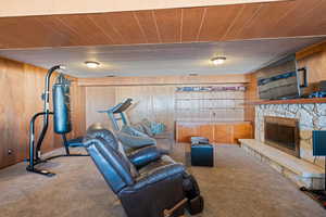 Living room featuring carpet floors, wood walls, wooden ceiling, and a stone fireplace