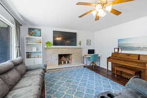 Living area featuring wood finished floors, ceiling fan, and a stone fireplace