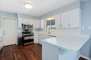 Kitchen with appliances with stainless steel finishes, dark wood-type flooring, a peninsula, and light countertops