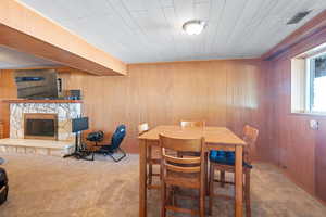 Carpeted dining area featuring wooden walls and a stone fireplace