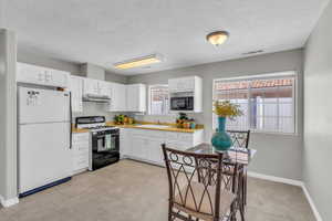 Kitchen with freestanding refrigerator, gas range oven, black microwave, white cabinets, and under cabinet range hood