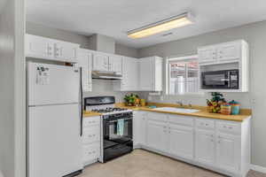 Kitchen featuring black appliances, under cabinet range hood, light countertops, white cabinets, and a textured ceiling