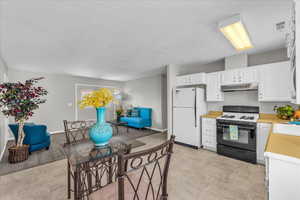 Kitchen with gas stove, freestanding refrigerator, under cabinet range hood, light countertops, and white cabinetry