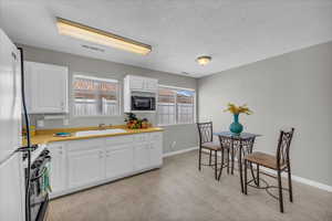 Kitchen with gas range oven, black microwave, light countertops, white cabinets, and a textured ceiling