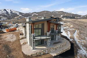 Snow covered back of property with a patio area, a mountain view, stone siding, and a chimney