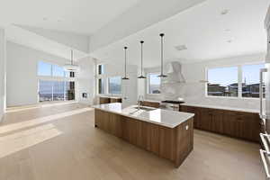 Kitchen featuring an island with sink, light wood-style floors, backsplash, open floor plan, and light stone countertops