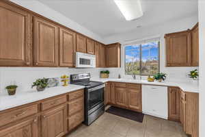 Kitchen featuring brown cabinets, white appliances, light tile patterned floors, and light countertops