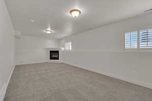Basement featuring a textured ceiling, a glass covered fireplace, and light colored carpet