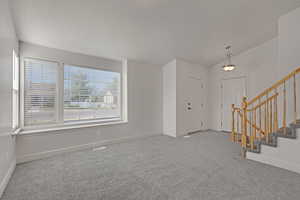 Carpeted foyer entrance featuring stairs and vaulted ceiling