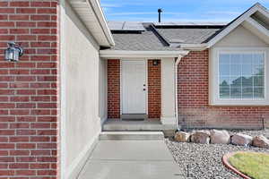 Property entrance featuring roof with shingles, brick siding, and solar panels