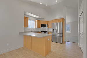 Kitchen featuring stainless steel appliances, a peninsula, light countertops, light tile patterned flooring, and decorative backsplash